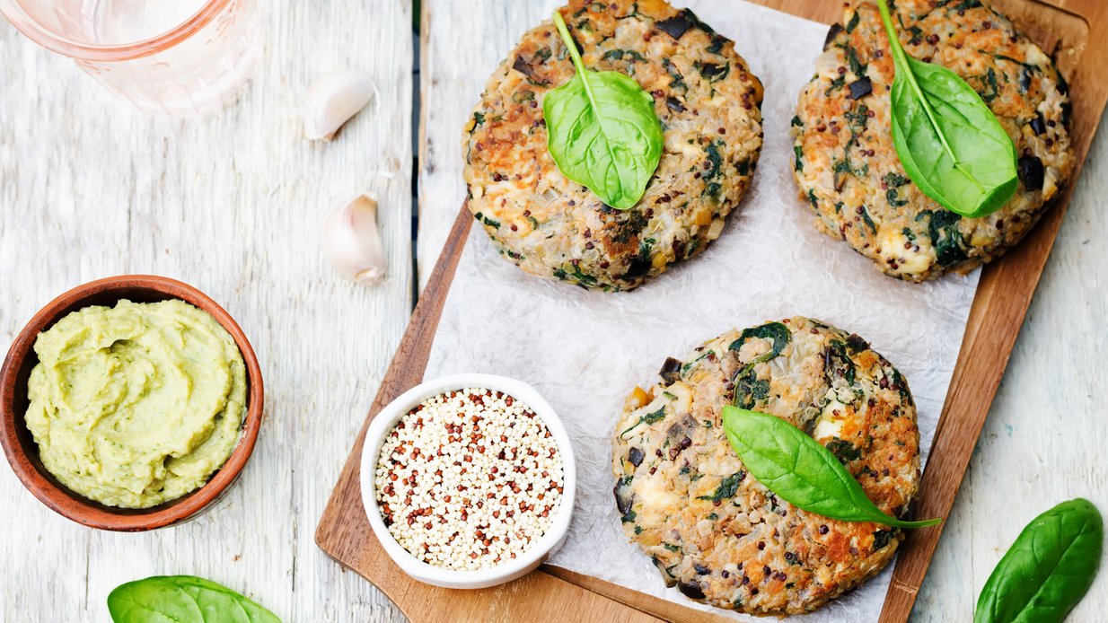 Drei vegetarisch-vegane Bratlinge mit zwei Dips und Kräutern garniert auf einem Holzbrettchen.